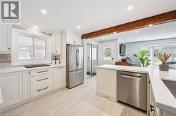 Contemporary kitchen featuring white shaker cabinetry, stainless steel appliances, light-toned tiled flooring, recessed lighting, and an exposed wood beam - 