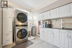 Laundry room featuring a stacked washer and dryer, extensive white cabinetry, a utility sink, and durable flooring - 