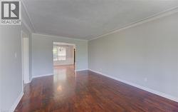 Spacious interior room featuring rich hardwood flooring, light gray walls, and crown molding - 