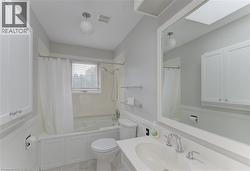 Bathroom featuring a combination tub/shower with white subway tile surround, white vanity cabinetry, a rectangular vanity mirror, and a skylight - 
