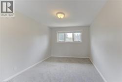 Neutral-toned interior room featuring light gray carpeting, a single window with white trim, and a ceiling-mounted light fixture - 