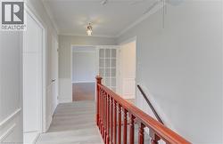 Upper-level hallway featuring light wood-finish flooring, white paneled walls, and crown molding. Stairs lead to finished basement with w/o - 