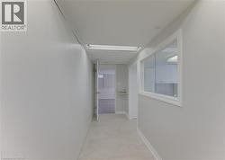Hallway featuring light-colored walls and flooring, a ceiling-mounted light fixture, and a framed interior window - 