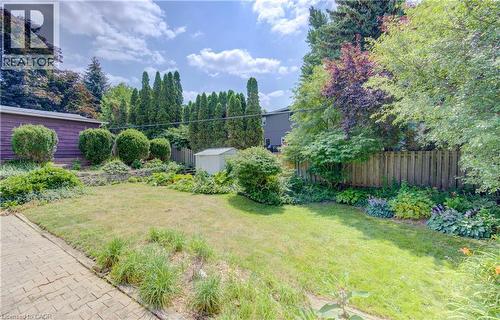 Expansive backyard featuring a brick paver patio, a manicured lawn, established shrubbery, mature trees, and a wooden privacy fence - 139 Trafalgar Avenue, Kitchener, ON - Outdoor