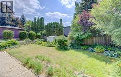 Expansive backyard featuring a brick paver patio, a manicured lawn, established shrubbery, mature trees, and a wooden privacy fence - 
