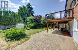 Expansive backyard featuring a raised wooden deck with railings, a lower patio area with patterned pavers, a manicured lawn, and mature perimeter trees - 