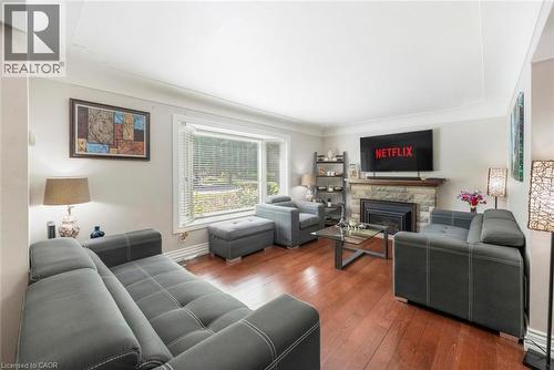 Spacious living area featuring wood-finish flooring, a stone-clad fireplace with a dark metal insert, and a large bay window - 1063 Joan Drive, Burlington, ON - Indoor Photo Showing Living Room With Fireplace