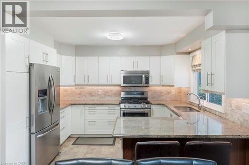 U-shaped kitchen featuring white cabinetry, stainless steel appliances, a stone tile backsplash, and granite countertops - 1063 Joan Drive, Burlington, ON - Indoor Photo Showing Kitchen With Stainless Steel Kitchen With Upgraded Kitchen