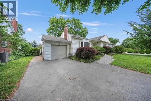 White siding exterior with an attached garage, a paved driveway, and mature landscaping - 1063 Joan Drive, Burlington, ON - Outdoor