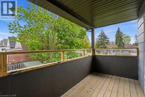 Covered outdoor patio featuring wood-finish flooring, a wood and glass panel railing, and a dark-paneled lower wall - 773 Lawrence Road, Hamilton, ON - Outdoor With Exterior