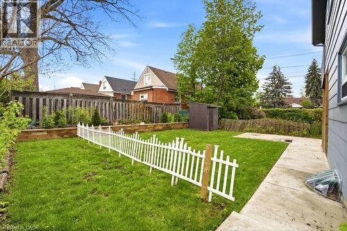 Expansive backyard featuring a lush green lawn, concrete patio, white picket fence, wooden privacy fence, and a storage shed - 773 Lawrence Road, Hamilton, ON - Outdoor With Backyard