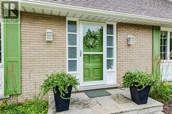 Brick exterior featuring a vibrant green entry door with a storm door, flanked by decorative sidelights and green louvered shutters - 