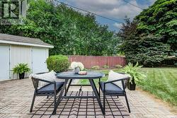 Expansive backyard patio featuring brick paver flooring, a detached shed with double doors, a manicured lawn, and mature perimeter trees - 