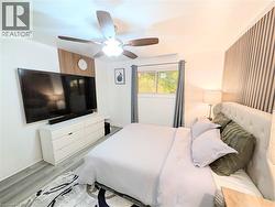 Bedroom featuring wood-finish flooring, a ceiling fan with integrated lighting, and a window with drapes - 