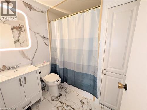 Bathroom featuring a white vanity with integrated sink, a rectangular illuminated mirror, and marble-patterned wall and floor tiling - 22 Riverdale Drive Unit# 1, Hamilton, ON - Indoor Photo Showing Bathroom