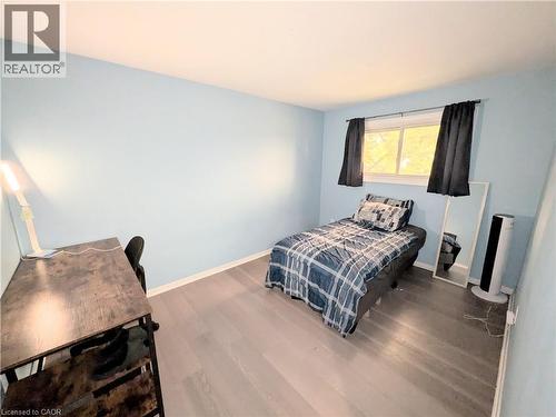 Light-filled interior space featuring a window with dark drapes, light blue walls, and wood-finish flooring - 22 Riverdale Drive Unit# 1, Hamilton, ON - Indoor Photo Showing Bedroom