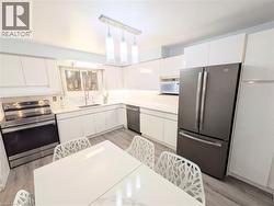 Contemporary kitchen featuring white cabinetry, light-toned countertops, and wood-finish flooring - 