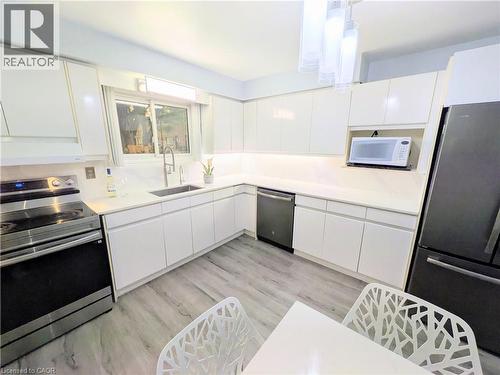 Modern kitchen featuring white cabinetry, light countertops, stainless steel appliances, wood-finish flooring, and a window with exterior views - 22 Riverdale Drive Unit# 1, Hamilton, ON - Indoor Photo Showing Kitchen
