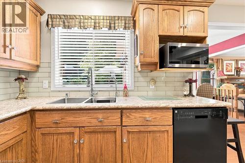 Kitchen workstation featuring wood cabinetry, light-toned countertops, a stainless steel double basin sink with a gooseneck faucet, a light subway tile backsplash, and an over-the-range microwave - 39 Everwood Run, Kitchener, ON - Indoor Photo Showing Kitchen With Double Sink