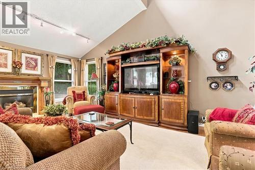 Vaulted ceiling living area featuring a fireplace with a wood mantel, track lighting, neutral carpeting, and multiple windows - 39 Everwood Run, Kitchener, ON - Indoor Photo Showing Living Room With Fireplace