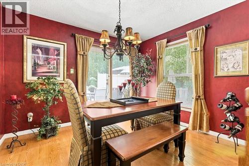 Dining area featuring wood-finish flooring, a contemporary chandelier, red wall treatment, and windows with blinds and drapes - 39 Everwood Run, Kitchener, ON - Indoor Photo Showing Dining Room