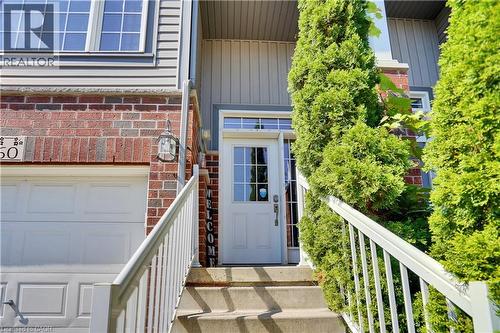 Brick and siding exterior featuring a white paneled garage door, concrete entry steps with white railings, a front door with integrated window, and established evergreen shrubbery - 60 Featherstone Street, Kitchener, ON - Outdoor