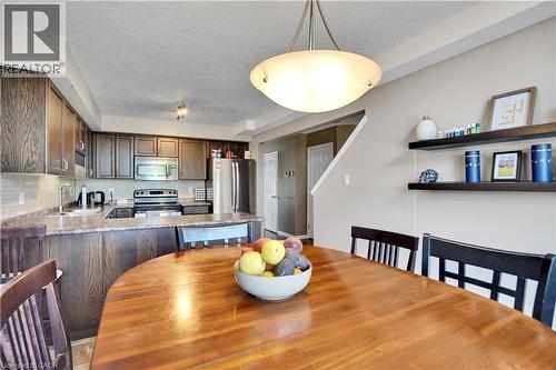 Open concept kitchen and dining area featuring wood-finish cabinetry, stainless steel appliances, a tiled backsplash, and a breakfast bar - 60 Featherstone Street, Kitchener, ON - Indoor Photo Showing Dining Room