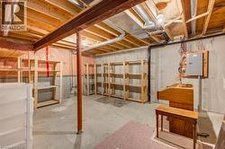 Unfinished basement featuring exposed wood joists, concrete flooring, perimeter shelving, and visible utility infrastructure including ductwork and electrical panel - 
