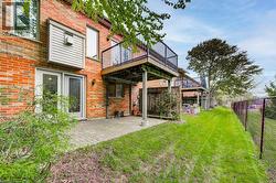 Expansive green space bordering the property, featuring a paved patio area, an elevated wood-finish deck with metal railings, and a brick exterior with sliding glass doors - 