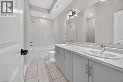 Bathroom featuring a double vanity with undermount sinks, a large wall-mounted mirror, and a bathtub/shower combination with tiled surround - 