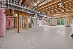 Unfinished lower level featuring exposed ceiling joists and ductwork, concrete flooring, a sliding glass door, and a single window - 