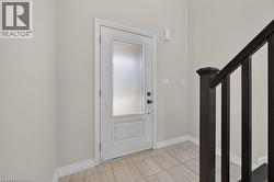 Entryway featuring a white door with a frosted glass insert, dark wood-finish staircase railing, light-toned tile flooring, and neutral wall paint - 