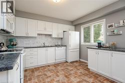 Kitchen featuring white cabinetry, dark countertops, a subway tile backsplash, white appliances, and brick-patterned flooring - 