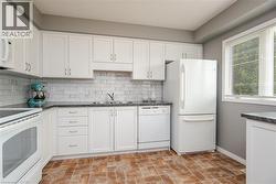 Kitchen featuring white cabinetry, dark countertops, white subway tile backsplash, and a double basin sink - 