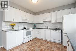 Kitchen featuring white cabinetry, dark speckled countertops, white subway tile backsplash, and brick-patterned flooring - 