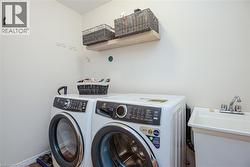 Dedicated laundry area featuring a utility sink with dual-handle faucet, a floating wood-finish shelf, and wall-mounted hooks - 