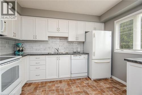 Kitchen featuring white cabinetry, dark countertops, white subway tile backsplash, and a double basin sink - 38 David Bergey Drive, Kitchener, ON - Indoor Photo Showing Kitchen