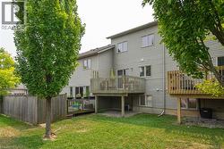 Rear exterior featuring two levels of light gray siding, a private wood deck, a patio on the ground level, mature trees, and a grass lawn - 