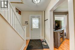 Foyer featuring wood-finish flooring, a white staircase with balusters, a white entry door with leaded glass, and a coat rack - 