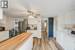 Kitchen featuring wood-finish flooring, white cabinetry, a central island with a wood-finish countertop, stainless steel appliances, and a ceiling fan with integrated lighting - 