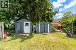 Spacious backyard featuring two storage sheds, a tiered wooden deck, and mature trees providing natural screening - 