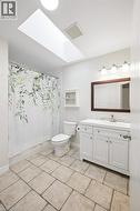Bathroom featuring a rectangular skylight, white vanity with a single sink and chrome faucet, and a wall-mounted light fixture - 