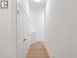Hallway featuring light wood-finish flooring, white walls, and multiple panel doors with brushed nickel hardware - 