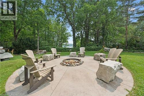 Circular concrete patio with a central stone-ringed fire pit, surrounded by Adirondack-style chairs and natural stone seating, with an Inukshuk stone feature - 410 Avenue Road, Cambridge, ON - Outdoor