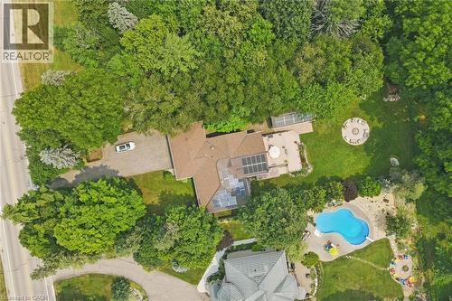 Spacious property featuring a large residence with a brown shingled roof, a substantial driveway, a circular patio with a fire pit, and extensive surrounding mature trees - 410 Avenue Road, Cambridge, ON - Outdoor With View