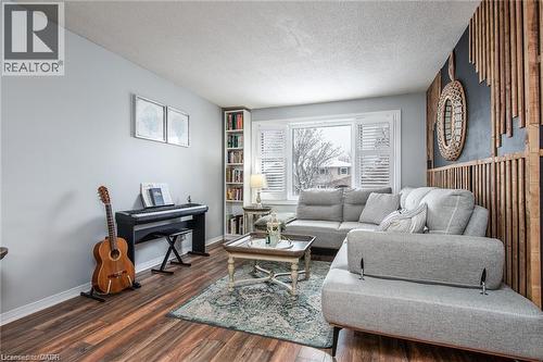 Spacious living area featuring wood-finish flooring, a built-in shelving unit, and a prominent bay window with white plantation shutters - 67 Pinemeadow Crescent, Waterloo, ON - Indoor Photo Showing Living Room