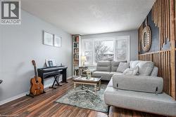 Spacious living area featuring wood-finish flooring, a built-in shelving unit, and a prominent bay window with white plantation shutters - 