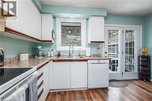Kitchen featuring wood-finish flooring, white cabinetry with brown trim, a built-in dishwasher, and a double patio door with gridded glass panels - 67 Pinemeadow Crescent, Waterloo, ON - Indoor Photo Showing Kitchen With Double Sink