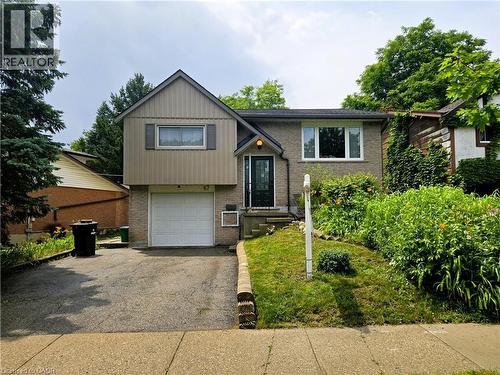 Split-level residence featuring a brick and vertical siding facade, an attached garage, and a sloped front yard with established plantings - 67 Pinemeadow Crescent, Waterloo, ON - Outdoor
