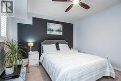Bedroom featuring a ceiling fan with integrated lighting, a contrasting accent wall, plantation shutters, and soft carpeting - 
